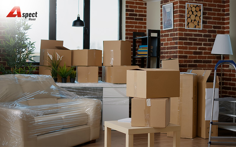 Living room packed for furniture moving with boxes and wrapped sofa for protection during relocation