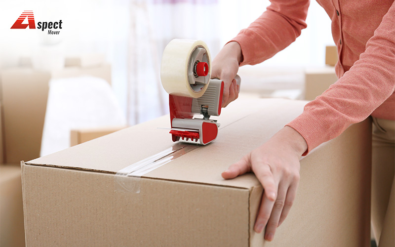 Person sealing a moving box with tape during house packing